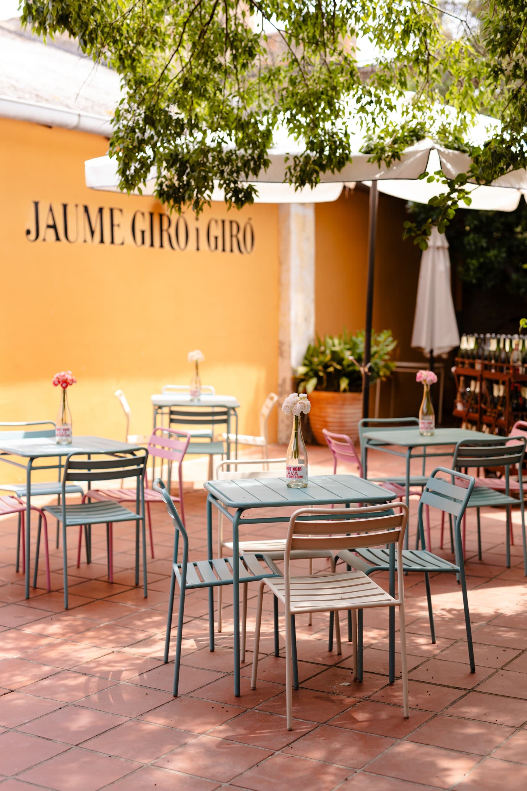 Sunny outdoor patio featuring colorful metal furniture and a white umbrella against a yellow wall.